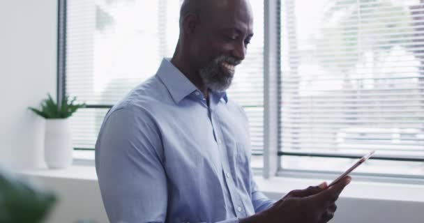 Smilende Afroamerikansk Forretningsmann Som Bruker Digital Nettbrett Står Ved Vinduet – stockvideo