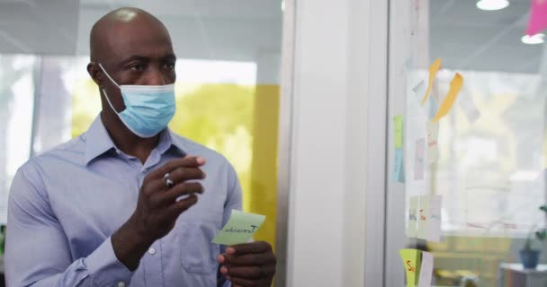 Afrikanischer Geschäftsmann Mit Gesichtsmaske Beim Brainstorming Und Legt Notizen Ins — Stockvideo