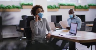 Yüzü maskeli çeşitli erkek ve kadın iş arkadaşları. Ofiste akıllı telefondan konuşan kadın. Covid 19 Coronavirüs salgını sırasında modern ofiste çalışan iş adamları..