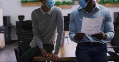 Yüz maskesi takmış çeşitli erkek ve kadın iş arkadaşları bürodaki belgelere bakıp konuşuyorlar. Covid 19 Coronavirüs salgını sırasında modern ofiste çalışan iş adamları..