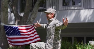 Beyaz bir oğlan elinde Amerikan bayrağı, bahçede üniformalı askeri babasına sarılıyor. Usta asker eve dönüş konsepti