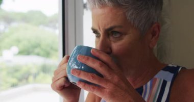 Kafkasyalı son sınıf öğrencisi kadın evde pencereden dışarı bakarken kahve içiyor. emekli çift yaşam tarzı konsepti