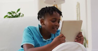 Evdeki kanepede otururken dijital tablet kullanırken gülümseyen Afrikalı Amerikalı çocuk. Aile, birliktelik ve mutluluk kavramı