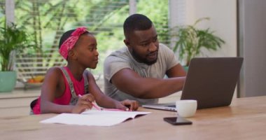 Afrikalı Amerikalı baba dizüstü bilgisayar kullanıyor ve kızına ev ödevlerinde yardım ediyor. Aile, birliktelik ve mutluluk kavramı