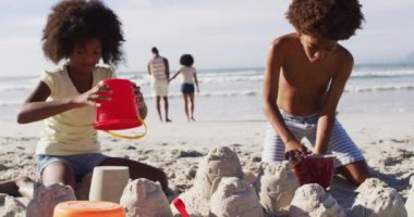 Afrikalı Amerikalı erkek ve kız kardeşler kumsalda kumla oynuyorlar. sağlıklı açık hava eğlence zamanı deniz kenarında.