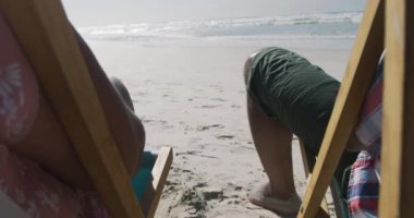 Kıdemli Afro-Amerikan çift güneşli yataklarda oturuyor ve sahilde el ele tutuşuyorlar. sağlıklı açık hava eğlence zamanı deniz kenarında.