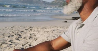 Kıdemli Afro-Amerikan adam sahilde oturmuş manzarayı seyrediyor. sağlıklı açık hava eğlence zamanı deniz kenarında.