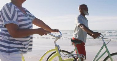 Gülümseyen kıdemli Afrikalı Amerikalı çift sahilde bisikletle yürüyor. sağlıklı açık hava eğlence zamanı deniz kenarında.