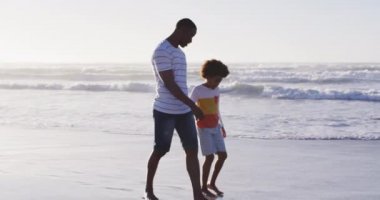 Afrikalı Amerikalı baba ve oğlu sahilde yürüyor ve el ele tutuşuyorlar. sağlıklı açık hava eğlence zamanı deniz kenarında.