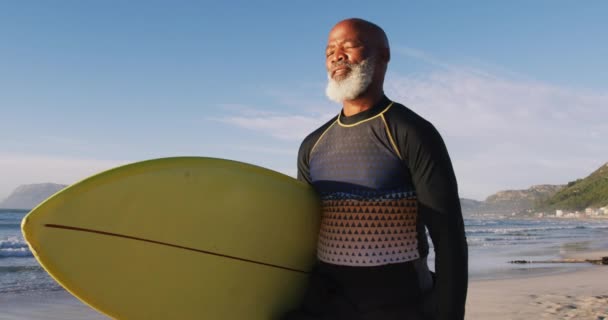 Senior Afroameričan kráčí se surfařem na pláži. zdravý venkovní volný čas u moře.