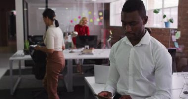 Afro-Amerikalı işadamı açık alanda kameraya bakarak masasında oturuyor. Modern bir ofiste iş..