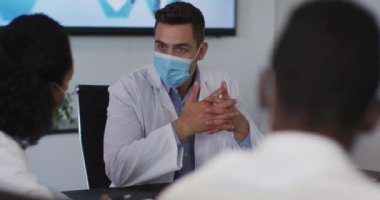 Maske takan melez erkek doktor toplantı odasında jest yaparken sunum yapıyor. Covid 19 Coronavirus salgını sırasında tıp uzmanları iş başında..