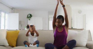 Mutlu Afro-Amerikan anne ve kızı kanepede oturup evde yoga yapıyor. Karantina süresince evde tek başına kalmak..