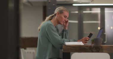 Kafkasyalı iş kadını masada dizüstü bilgisayar ve akıllı telefon kullanarak merak ediyor. Modern bir ofiste iş..