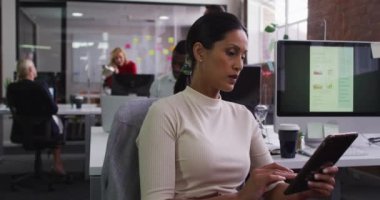 Karışık ırk işkadını açık alanda masada oturup tablet gülümseme kullanıyor. Modern bir ofiste iş..