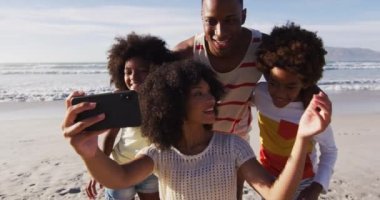 Afrika kökenli Amerikalı aileler ve çocukları sahilde akıllı telefonlarıyla selfie çekiyorlar. Aile deniz kenarında boş vakit geçirir..