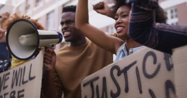 抗議の間に拳を上げる他の人々とメガホンを使って叫んでいるアフリカ系アメリカ人の男性 デモ行進中の平等な権利と正義の抗議者は — ストック動画