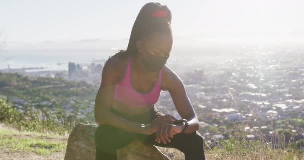 Mujer Afroamericana Usando Mascarilla Usando Smartwatch Mientras Está Sentada Una — Vídeos de Stock