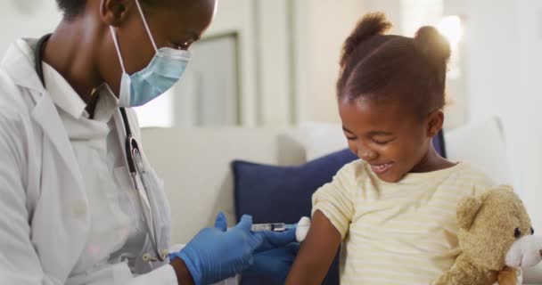 Afroamerikanische Ärztin Mit Gesichtsmaske Gibt Lächelnden Mädchen Hause Eine Covid — Stockvideo