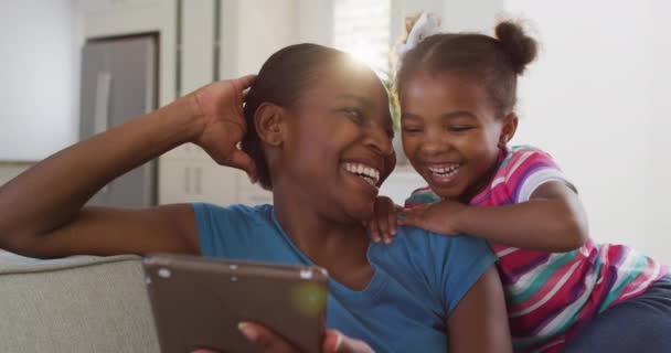 快乐的非洲裔美国母亲和女儿坐在沙发上 用数字平板电脑和笑声 隔离隔离隔离期间待在家里 — 图库视频影像