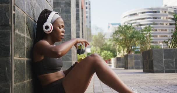 Mujer Afroamericana Haciendo Ejercicio Aire Libre Usando Auriculares Inalámbricos Bebiendo — Vídeos de Stock