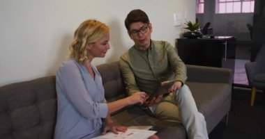 Asyalı bir adam ve beyaz bir kadın ofiste koltukta oturmuş dijital tablet üzerinde tartışıyorlar. ofis ve iş konsepti