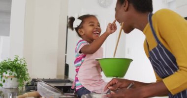 Mutlu Afro-Amerikan anne ve kızı önlük giyip mutfakta yemek yaparken eğleniyorlar. Karantina süresince evde tek başına kalmak..