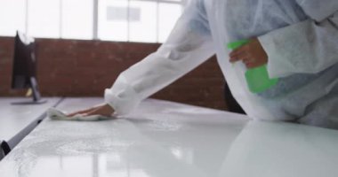 Temizleyicinin orta kısmı koruyucu tulum giyip ofisi ve mobilyaları dezenfekte ediyor. Coronavirus covid 19 salgını sırasında işyerinde hijyen.