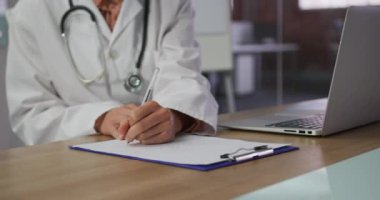 Maskeli beyaz kadın doktor toplantı odasında oturmuş notlar alıyor. Covid 19 Coronavirus salgını sırasında tıp uzmanları iş başında..