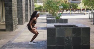 Dışarıda egzersiz yapan, kablosuz kulaklık takan, şehirde hoplayan Afrikalı Amerikalı bir kadın. sağlıklı açık hava yaşam tarzı fitness eğitimi.