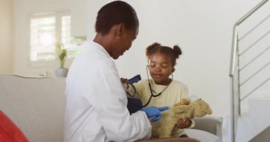 Tıbbi ev ziyareti sırasında steteskop kullanan ve gülümseyen Afrikalı Amerikalı bir kız. Tıbbi uzman hasta ev ziyareti yapıyor.