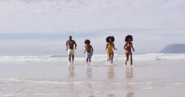 Afrika kökenli Amerikalı ebeveynler ve plajda koşan iki çocuk. Aile deniz kenarında boş vakit geçirir..