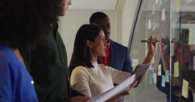 Toplantı odasındaki çeşitli meslektaşlar karışık ırk işkadınlarının cam duvara notlar yazması. Modern bir ofiste iş..