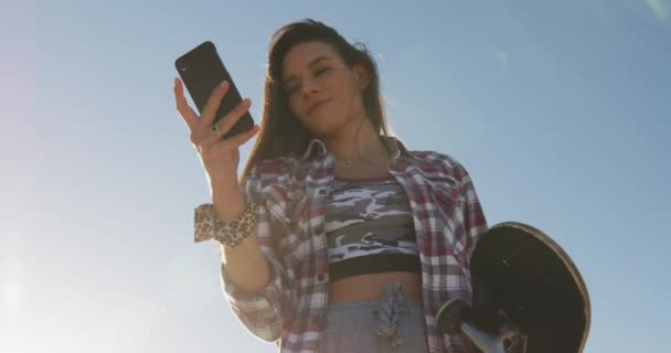 Mujer Caucásica Sonriente Usando Teléfono Inteligente Sosteniendo Monopatín Parque Skate — Vídeos de Stock