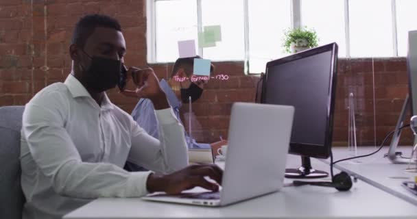 Africký Podnikatel Masce Sedí Stole Používá Notebook Který Mluví Smartphonu — Stock video