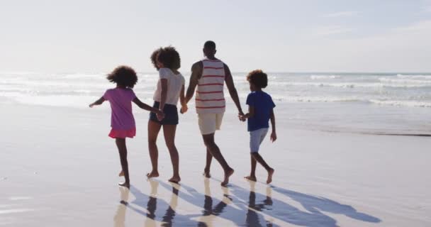 アフリカ系アメリカ人の両親と彼らの子供たちはビーチを歩いて手をつないでいます 海のそばの家族のアウトドアレジャータイム — ストック動画