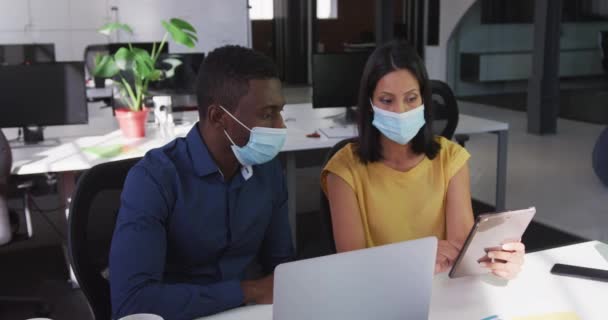 タブレットを使用して机に座って顔マスクを身に着けている多様な男性と女性のビジネス同僚 現在のオフィスで働いています19年のコロナウイルスの大流行の間 — ストック動画