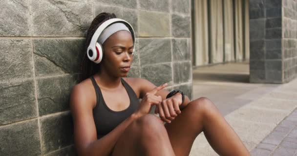 African American Woman Exercising Outdoors Wearing Wireless Headphones Using Smartwatch — Stock Video