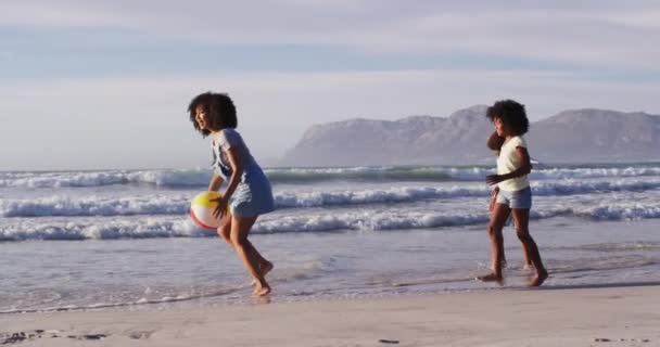 アフリカ系アメリカ人の母親と彼女の子供たちがビーチでボールで遊んでいる 海のそばの家族のアウトドアレジャータイム — ストック動画