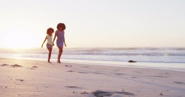 Afrika kökenli Amerikalı anne ve kız sahilde birlikte yürürken eğleniyorlar. Aile seyahati tatil eğlence konsepti