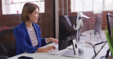 Asyalı iş kadını bilgisayarla masada oturuyor ve hapşırık koruyucusunun üzerinden dokümanları geçiriyor. Modern bir ofiste çalışıyorum.