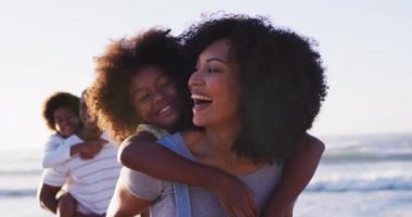 Afrika kökenli Amerikalı anne ve baba, sahildeki kızlarını ve oğullarını sırtlarına alıyorlar. Aile seyahati tatil eğlence konsepti