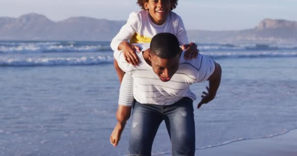 アフリカ系アメリカ人の父はビーチで息子にピギーバックに乗る 家族旅行休暇のコンセプト — ストック動画