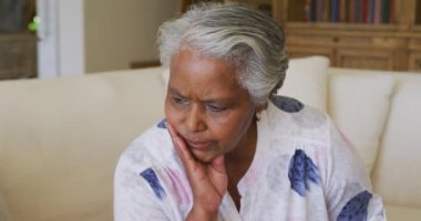Endiseli Afro-Amerikan son sinif kadinina yakin mesafede, elleri çenesinde, evde kanepede oturuyor. emeklilik son sınıf yaşam tarzı konsepti