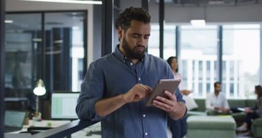 Gülümseyen karışık ırk işadamı, tablet kullanıyor ve kameraya bakıyor. Modern bir ofiste bağımsız yaratıcı iş.