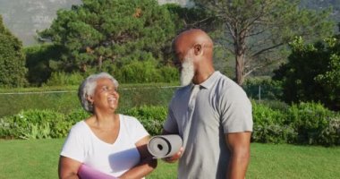 Bahçede dikilirken yoga minderleri tutan Afro-Amerikan son sınıf çifti portresi. emeklilik sporları ve aktif yaşlı yaşam tarzı.