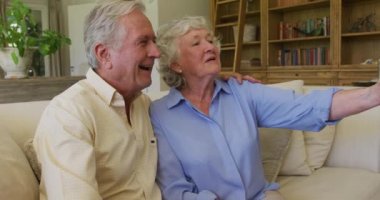 Gülümseyen Kafkasyalı son sınıf çifti evdeki kanepede oturmuş akıllı telefondan selfie çekiyor. emekli çift yaşam tarzı konsepti