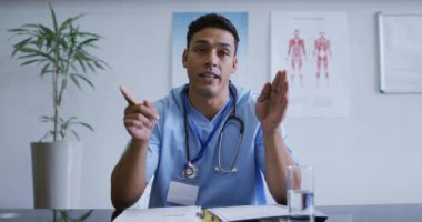 Masadaki melez erkek doktor görüntülü görüşme sırasında konuşuyor ve el kol hareketi yapıyor. Teletıp, karantina süresince çevrimiçi sağlık hizmetleri.