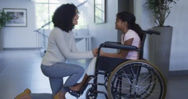 Afro-Amerikalı anne hastanede tekerlekli sandalyede oturan kızına sarılıyor. Sağlık ve Tıp Konsepti