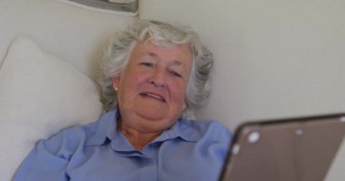 Evdeki kanepede yatarken dijital tablet kullanan beyaz bir kadın. emeklilik son sınıf yaşam tarzı konsepti